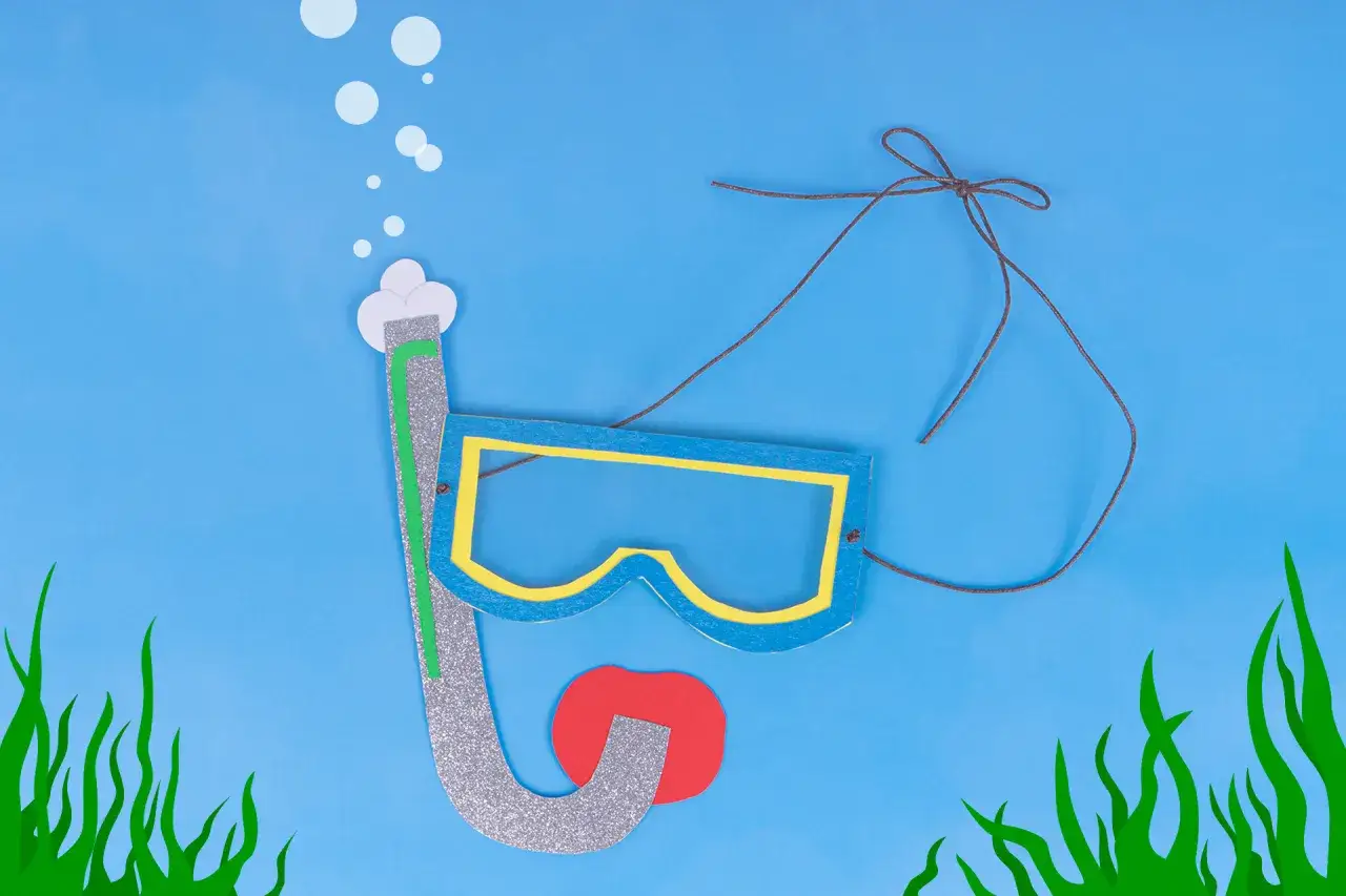 Bunte Bastelarbeit: Eine Taucherbrille mit Schnorchel und roten Lippen, umgeben von Seegras und Luftblasen.