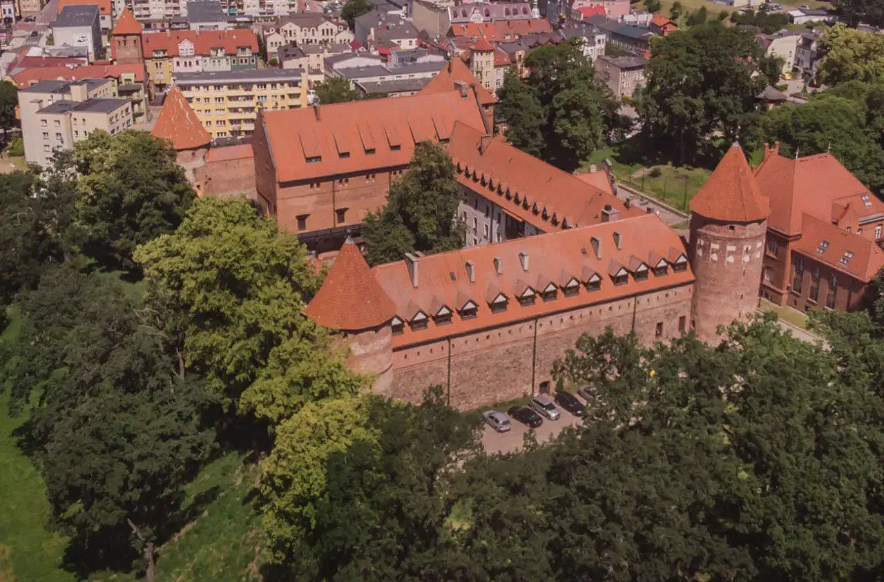 Zamek w Bytowie, otoczony zielenią, z czerwonymi dachami i kamiennymi murami, prezentuje się majestatycznie.