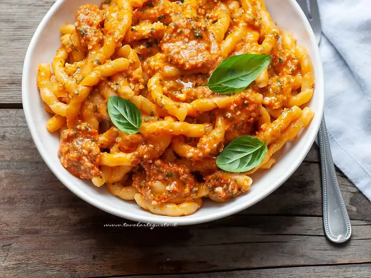 Un piatto invitante di busiate alla trapanese, condite con un sugo rosso ricco e guarnite con foglie di basilico fresco.