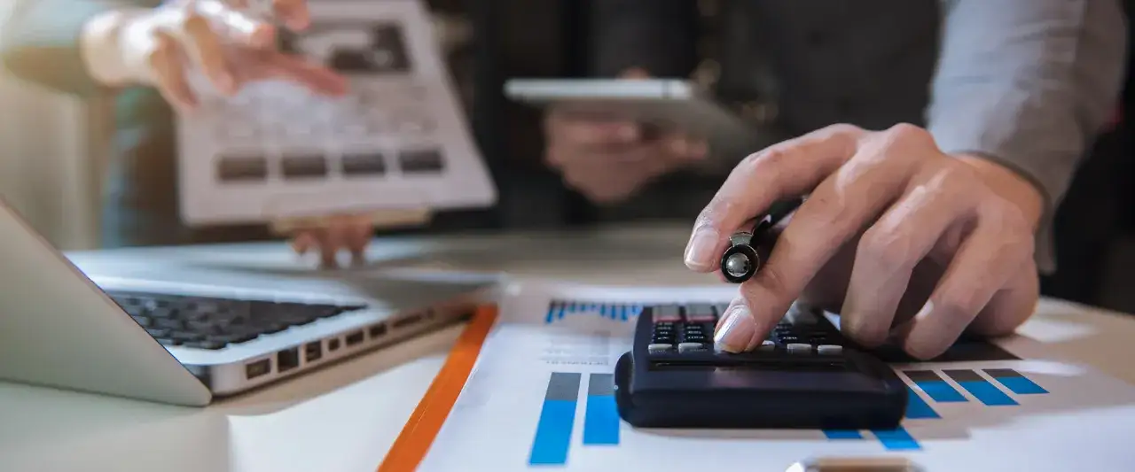 Manos trabajando en calculadora y port&aacute;til, analizando gr&aacute;ficos. Ideal para quienes cursan un grado superior administraci&oacute;n y finanzas online.
