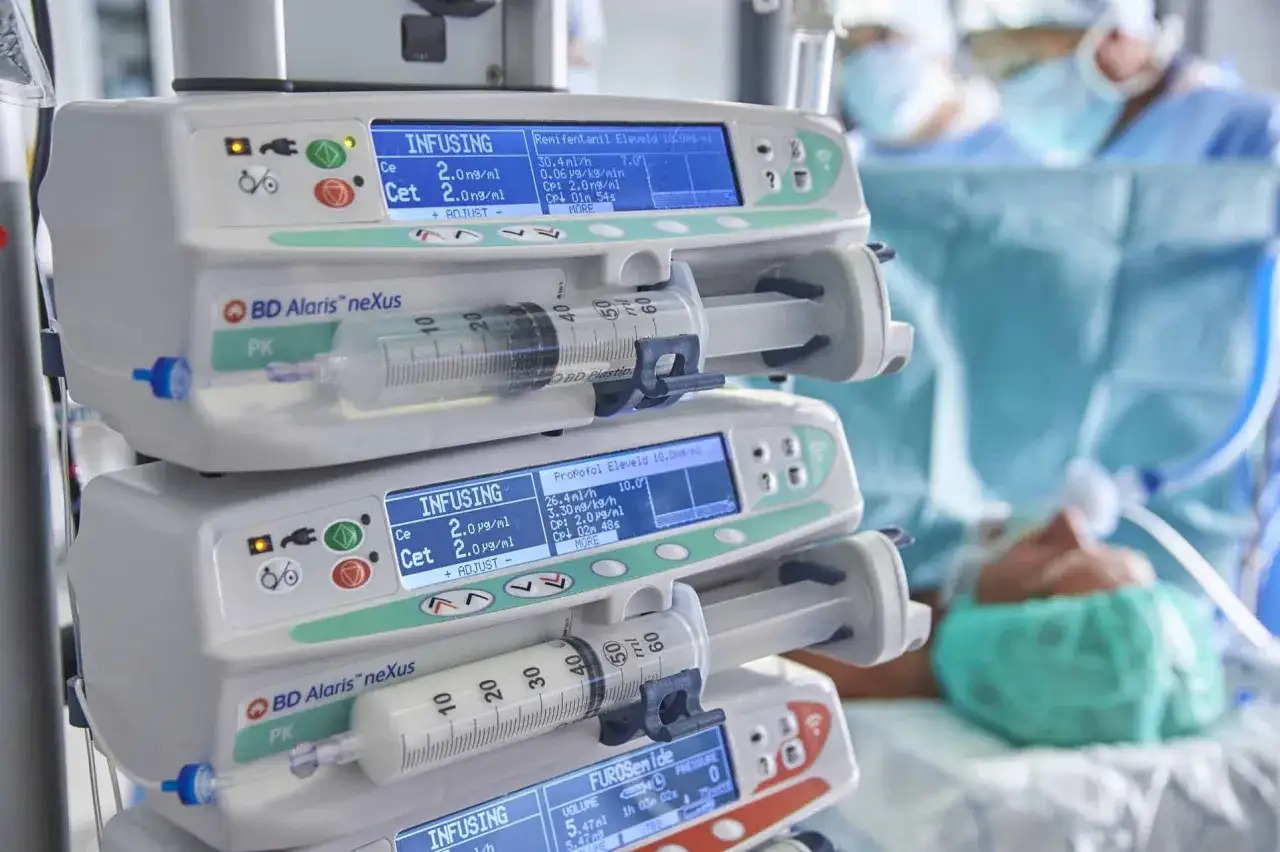 Pompy infuzyjne BD Alaris neXus z lekami, w tym propofol, w tle pacjent pod znieczuleniem.