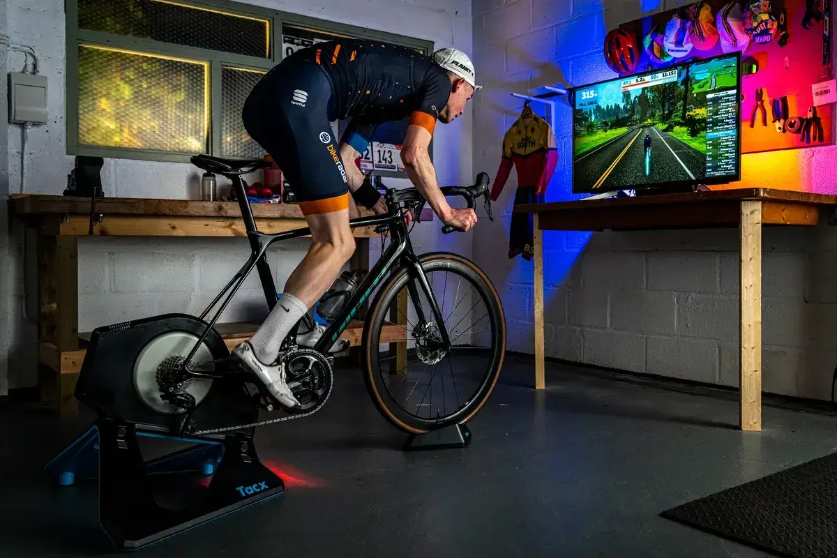 A cyclist is getting started with Zwift, riding a bike on a trainer in front of a screen displaying the virtual world.