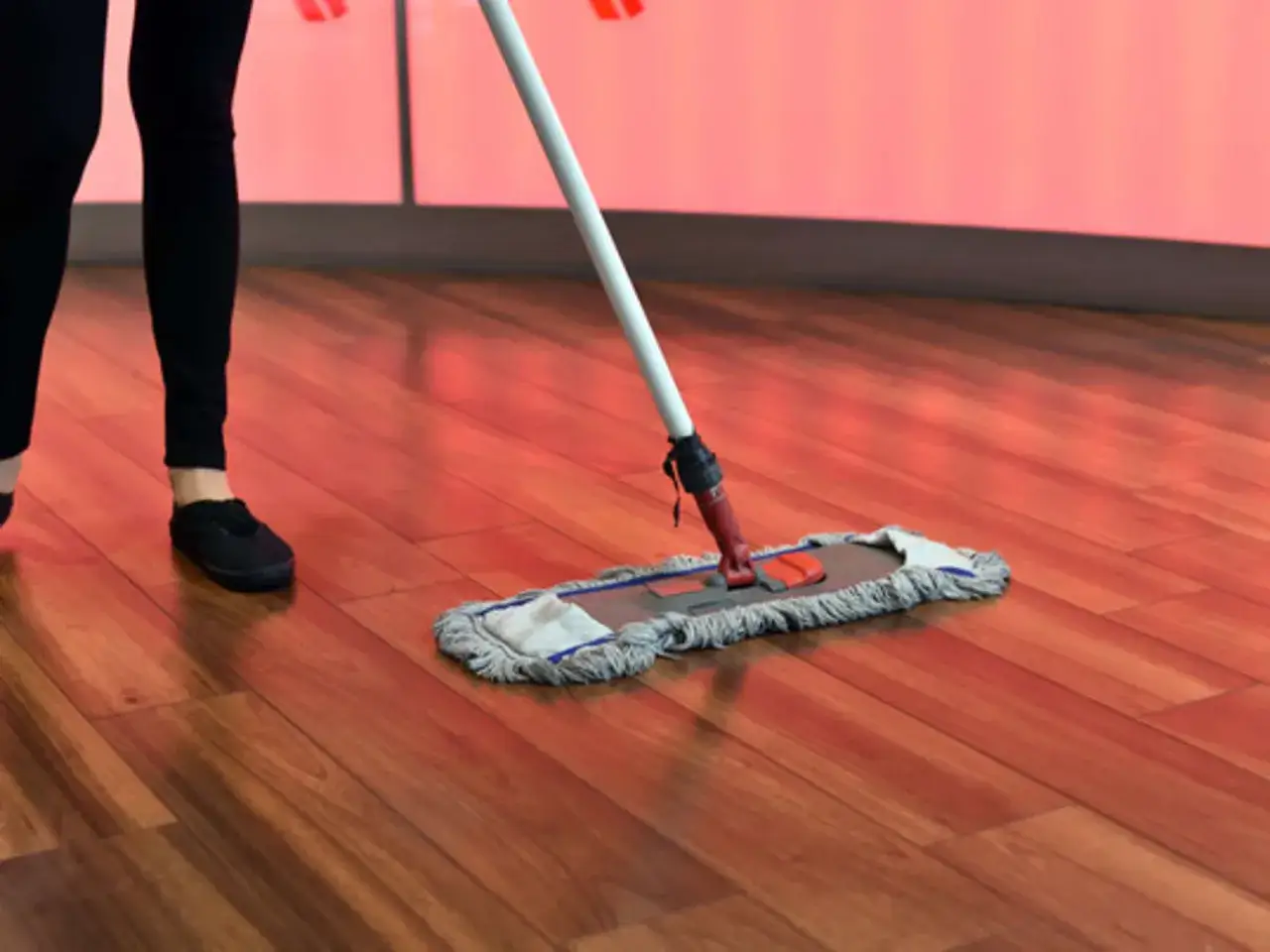 Person reinigt mit einem Mopp den glänzenden Parkettboden.