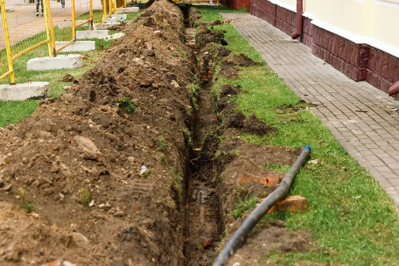 Wykopany r&oacute;w melioracyjny w granicy działki, z widoczną rurą i ziemią usypaną obok.