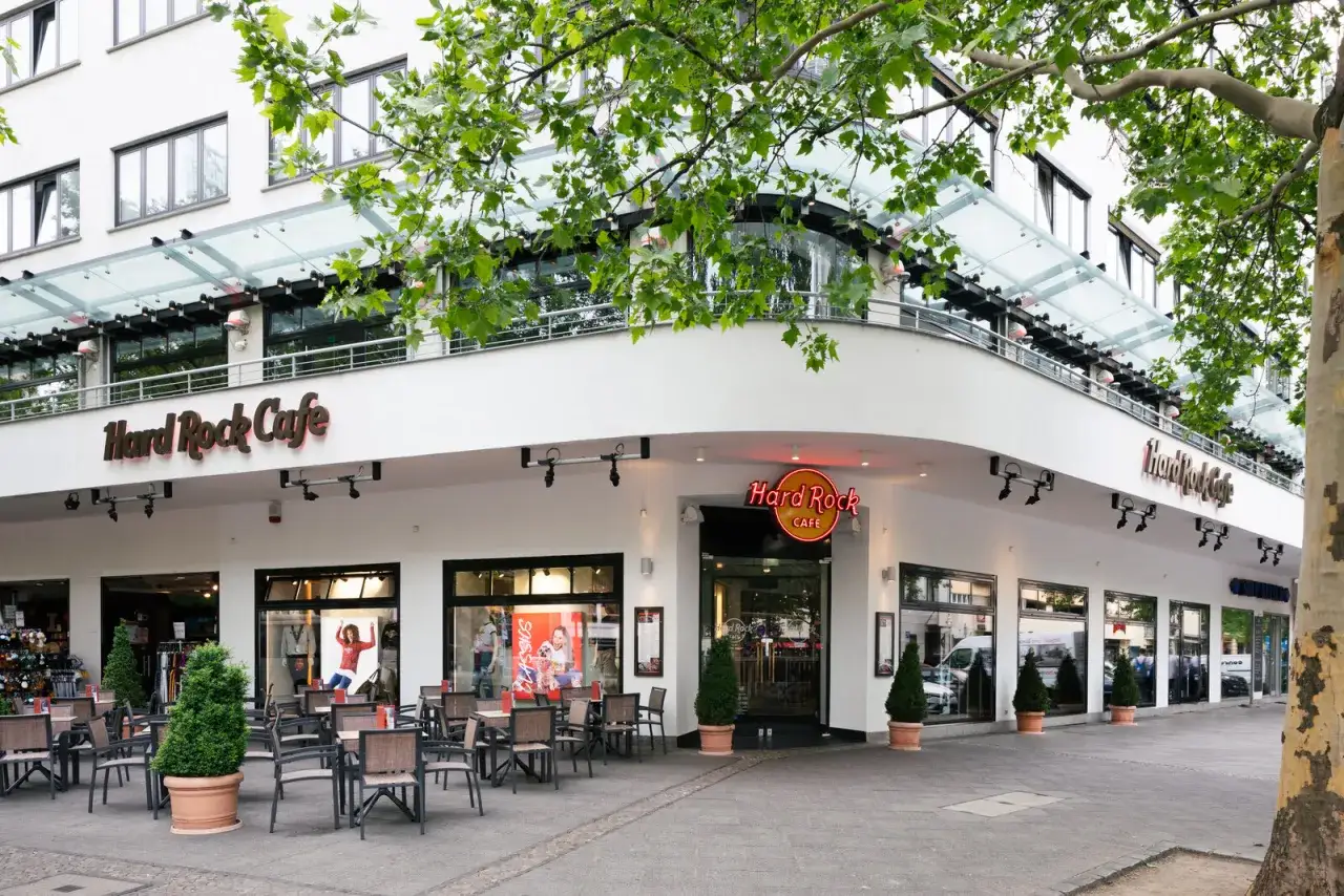 Das Hard Rock Cafe Berlin mit Au&szlig;enbestuhlung und gr&uuml;nen B&auml;umen davor.