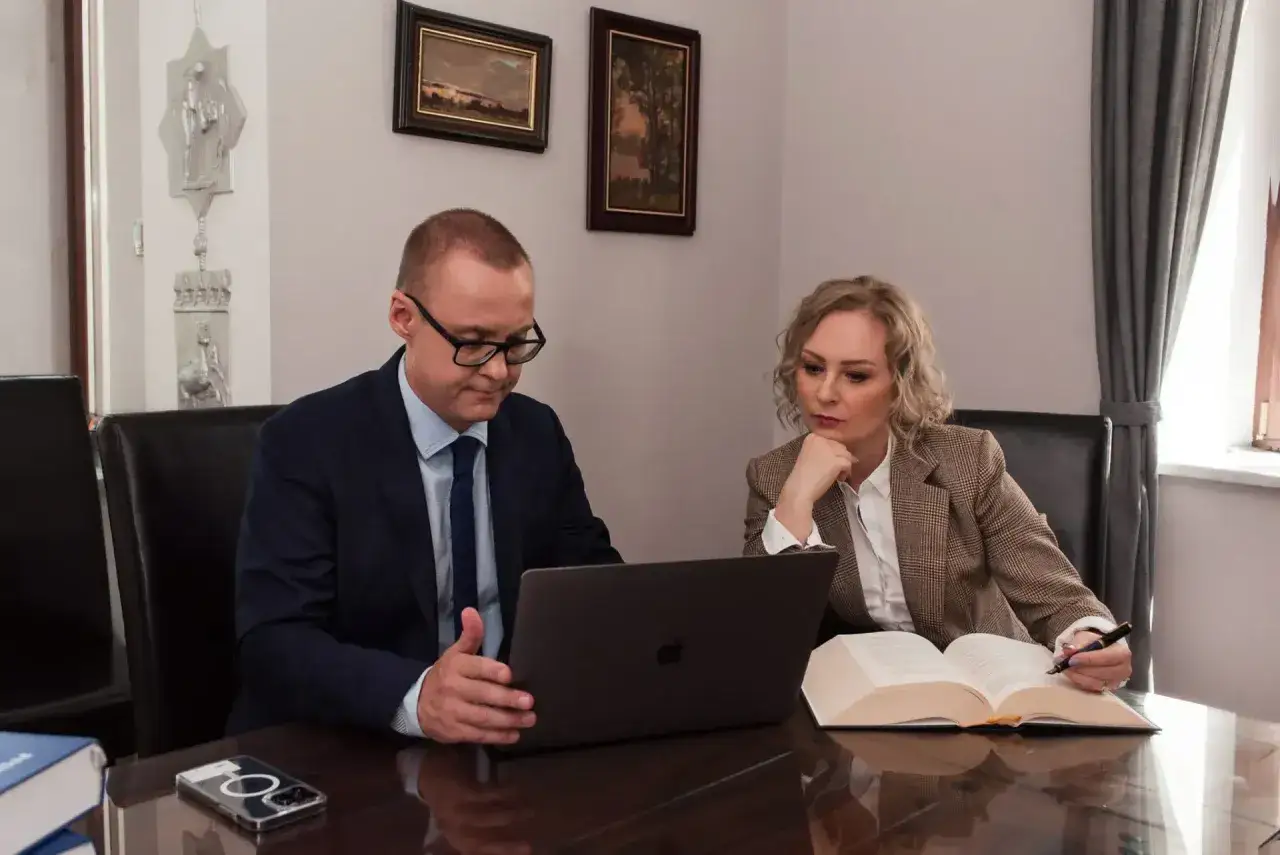Mężczyzna i kobieta w garniturach analizują dokumenty przy biurku.
