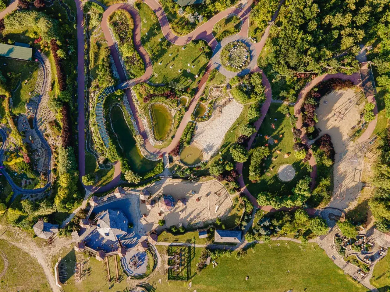 Widok z lotu ptaka na park pełen zieleni, ścieżek, stawów i placów zabaw. Tu właśnie są magiczne ogrody, gdzie dzieci mogą się bawić.