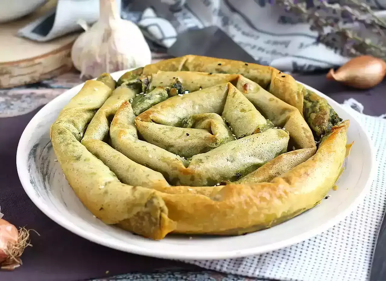 Złocisty borek ze szpinakiem, zwinięty w spiralę, kusi aromatem. Na talerzu, obok czosnku i cebulki, czeka na spróbowanie.