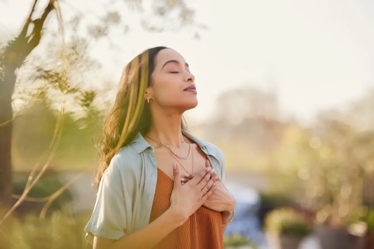 A woman with eyes closed and hands on her chest breathes deeply, embodying compassion and understanding as she connects with herself and the world around her.