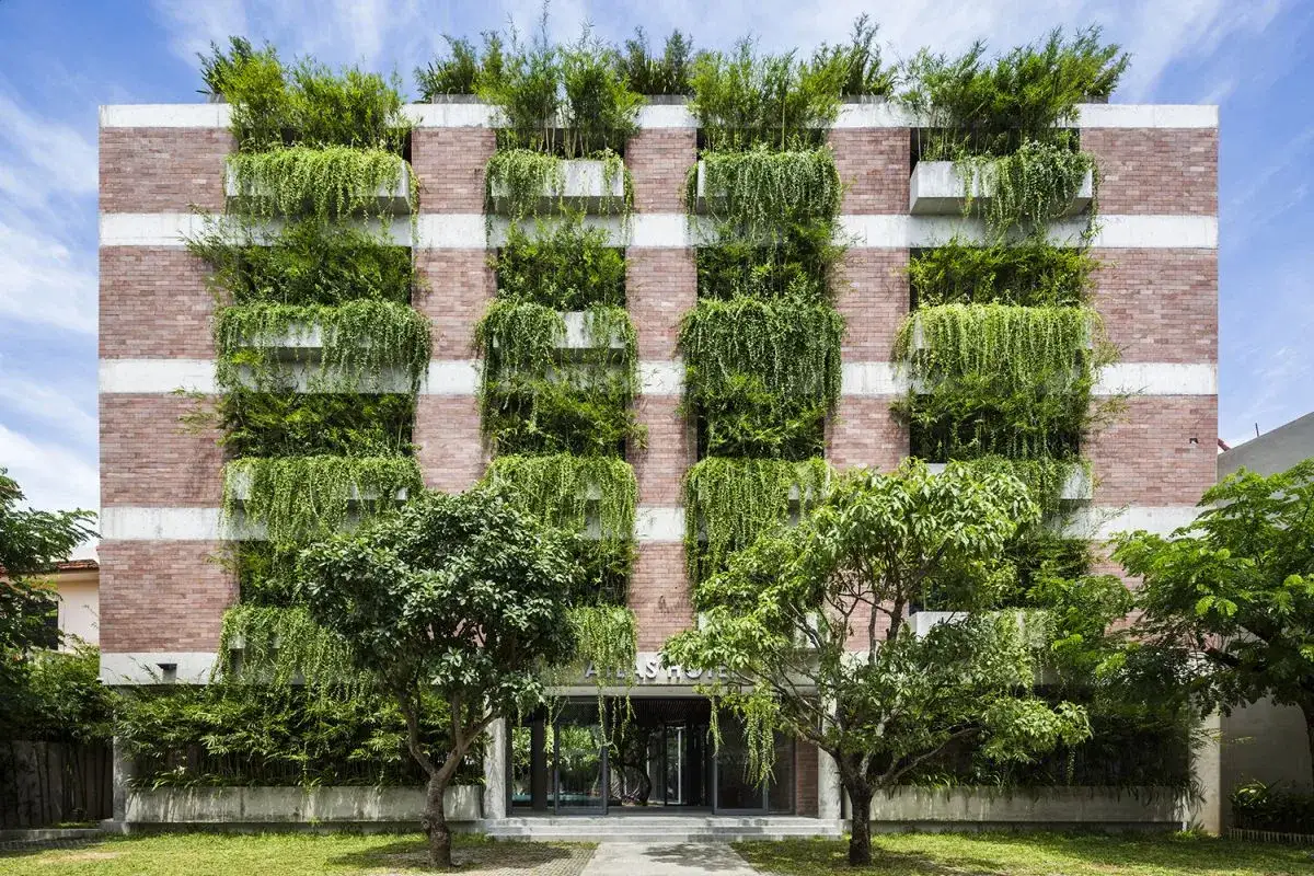 Edificio moderno con una **parete verde** lussureggiante, mattoni a vista e balconi pieni di piante che scendono a cascata.