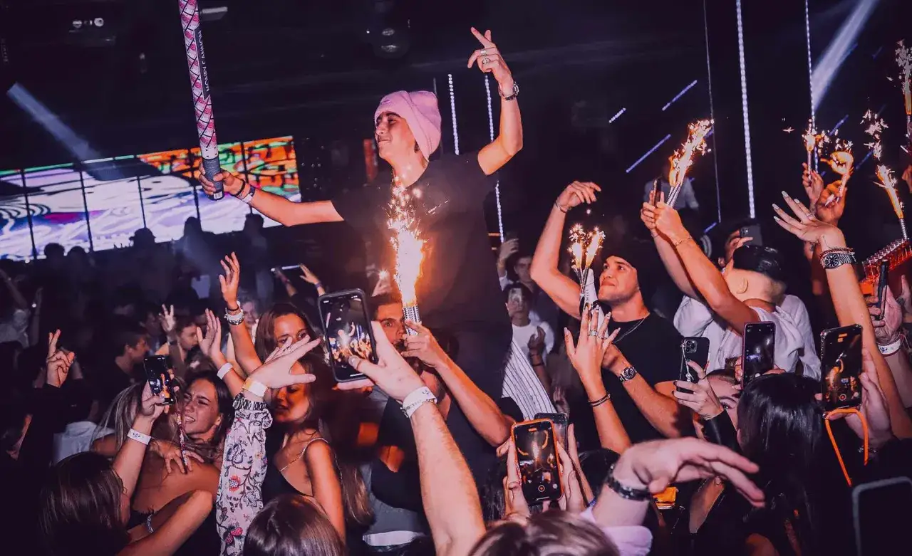Ragazzi festeggiano in una discoteca di Barcellona, con bengala e smartphone per immortalare la serata.