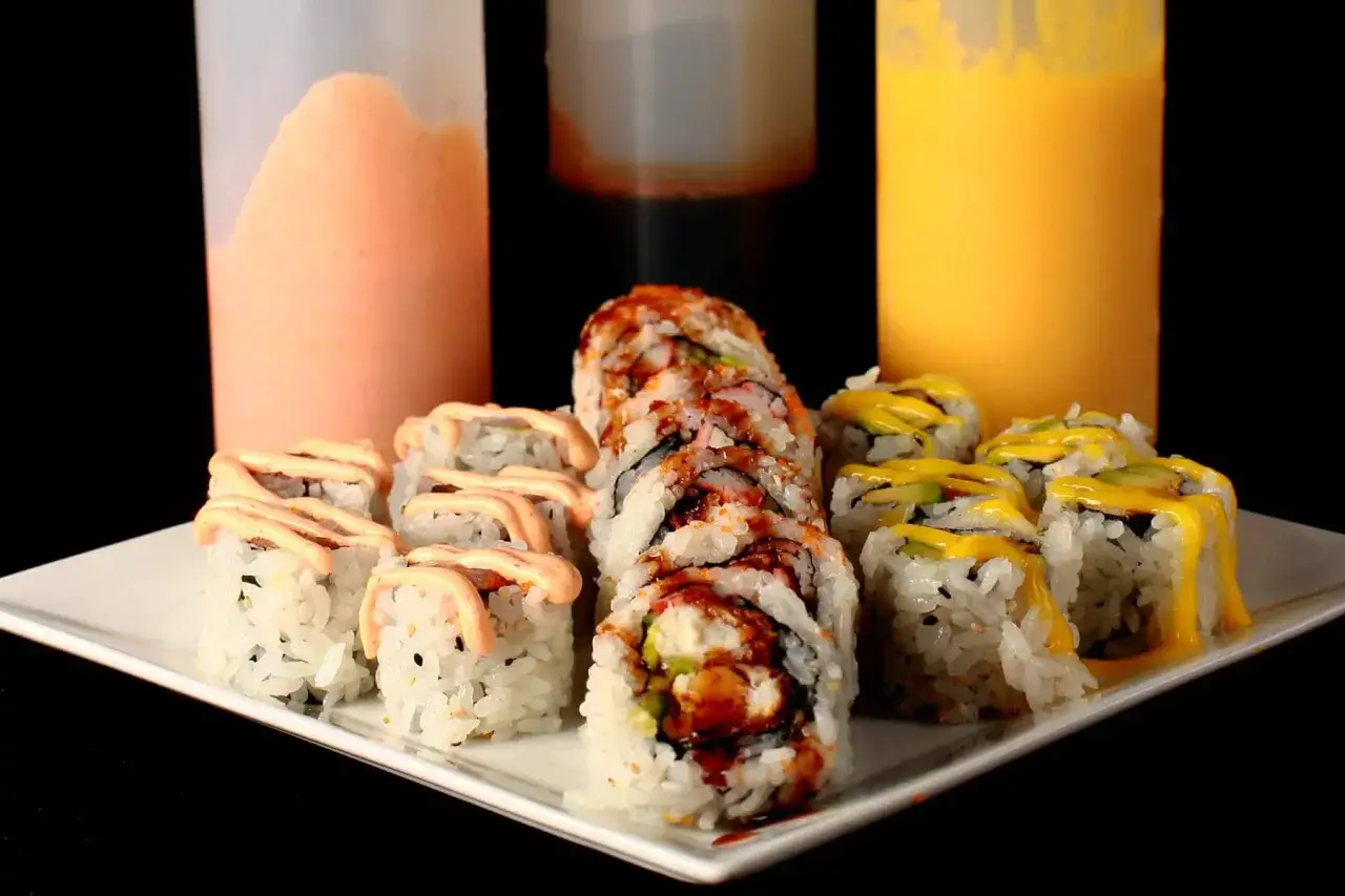 Różne rodzaje sushi z butelek z kremowym, pomarańczowym i żółtym sosem do sushi.