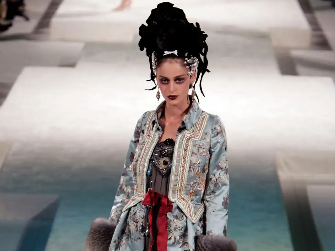 Mannequin portant une veste orn&eacute;e de broderies florales, un style audacieux d'un designer v&ecirc;tement. Chevelure haute et maquillage dramatique.