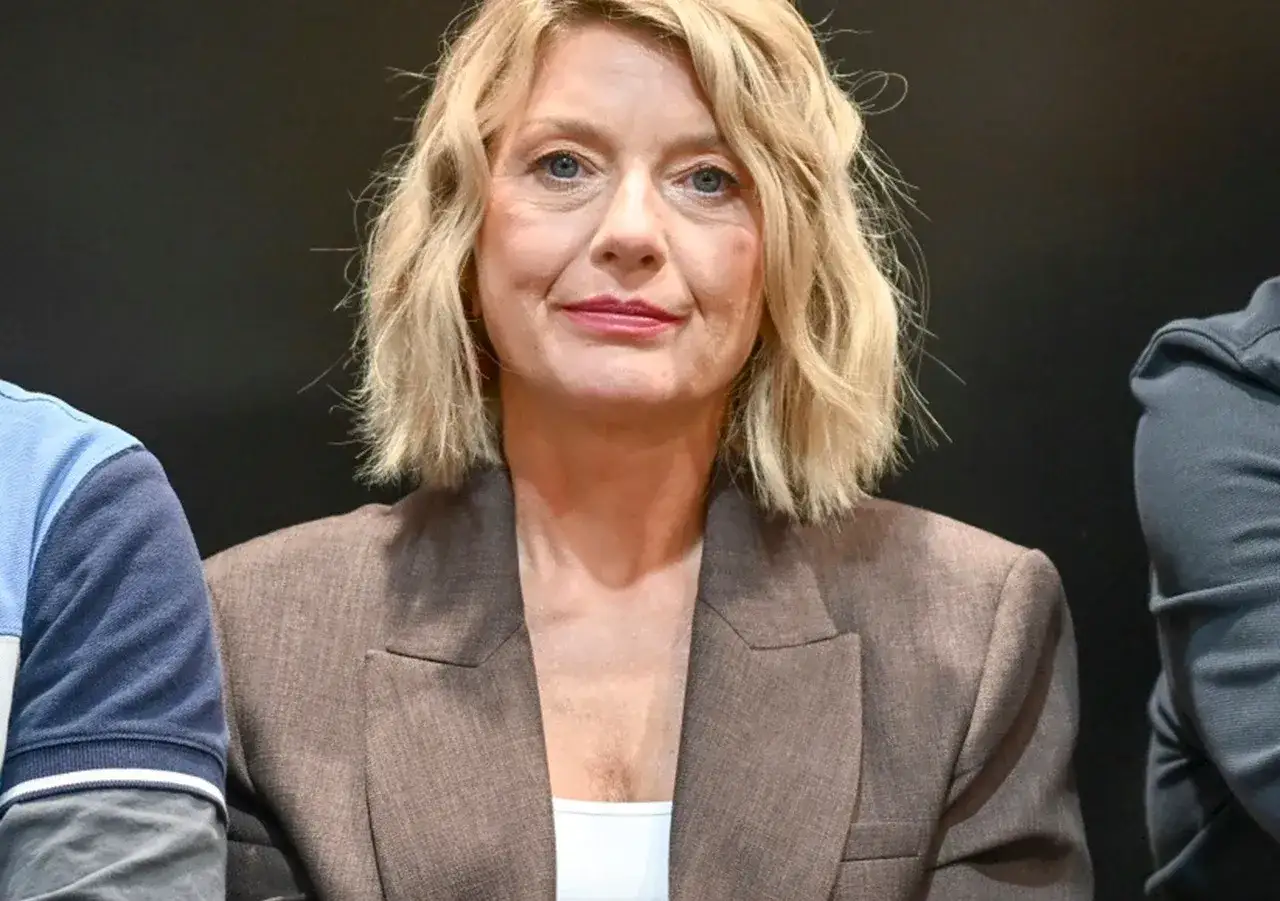 Kobieta z blond włosami w brązowej marynarce, uśmiecha się. Ile lat ma Edyta Olszówka? Trudno zgadnąć, wygląda świetnie!