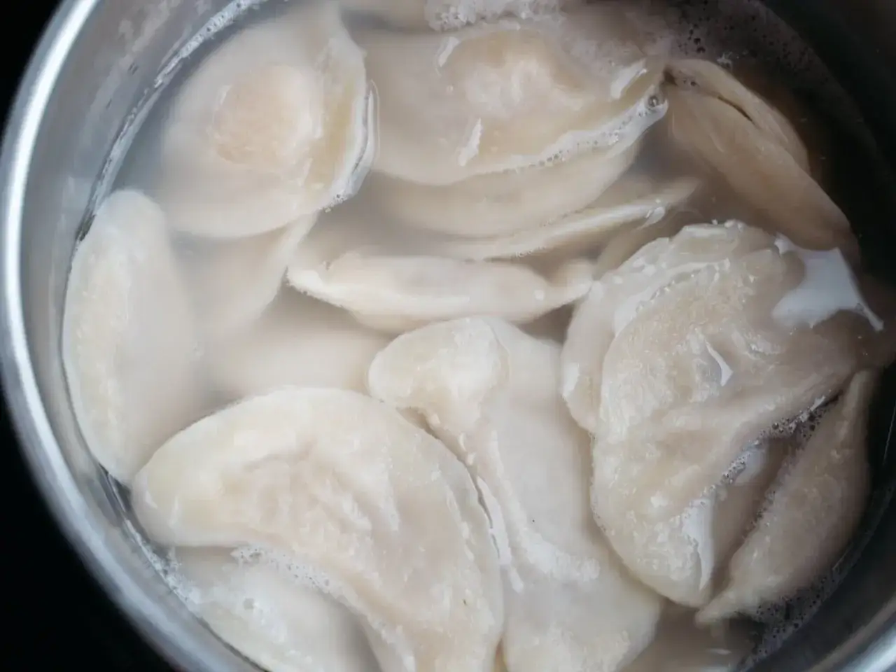 Jak ugotować pierogi? W garnku bulgocze woda, w której gotują się świeżo ulepione pierogi.