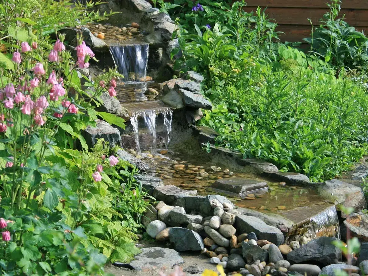 Kleine Kaskaden beleben diesen Garten. Tolle wasserfall garten ideen mit rosa Bl&uuml;ten und &uuml;ppigem Gr&uuml;n.