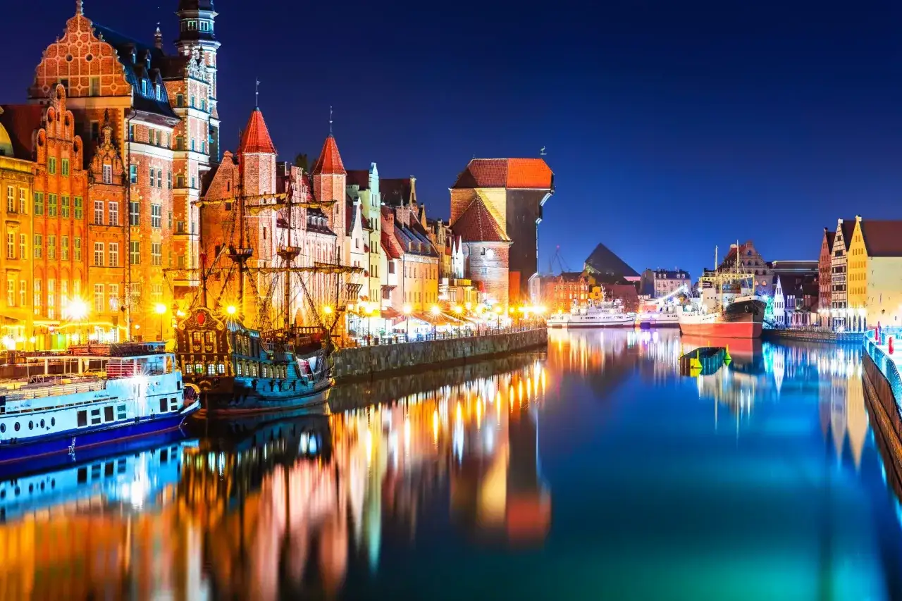 Nocny Gdańsk zachwyca. Widać zabytkowe kamienice, żaglowiec i Żuraw. Ciekawe ciekawostki o Gdańsku czekają na odkrycie nad Motławą.