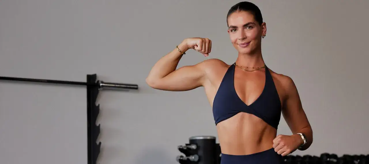 Kobieta w siłowni pokazuje biceps. Zastanawiasz się, ile cardio na redukcji jest optymalne?