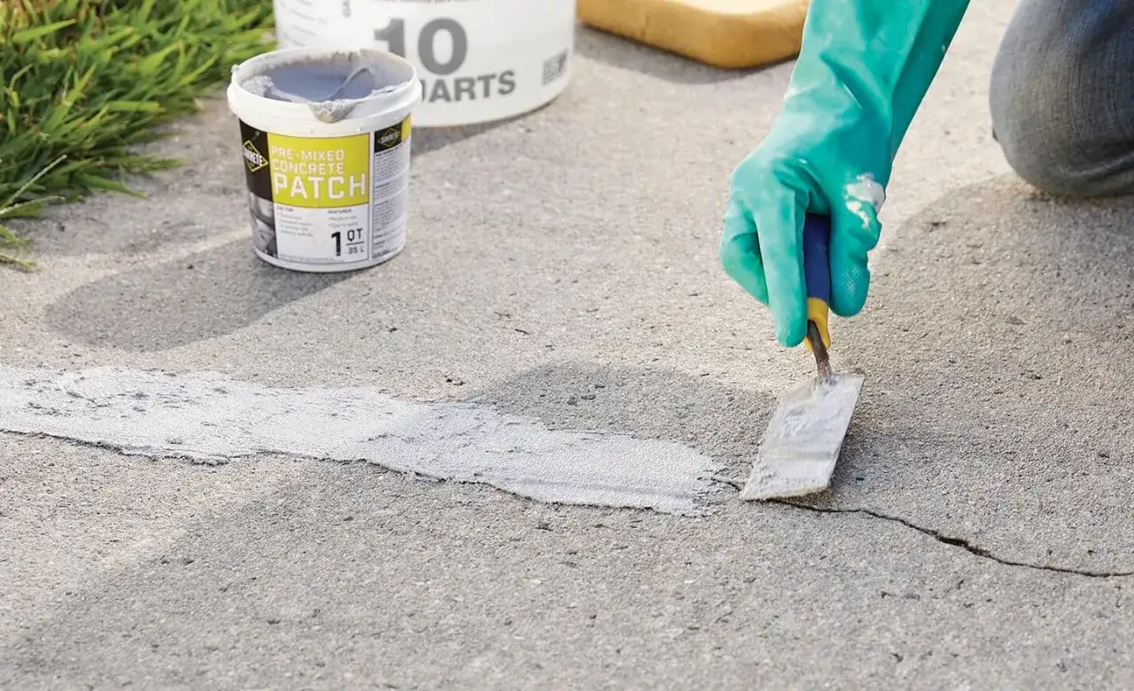 Persona con guantes verdes aplica masilla para reparar suelo de hormigón exterior.