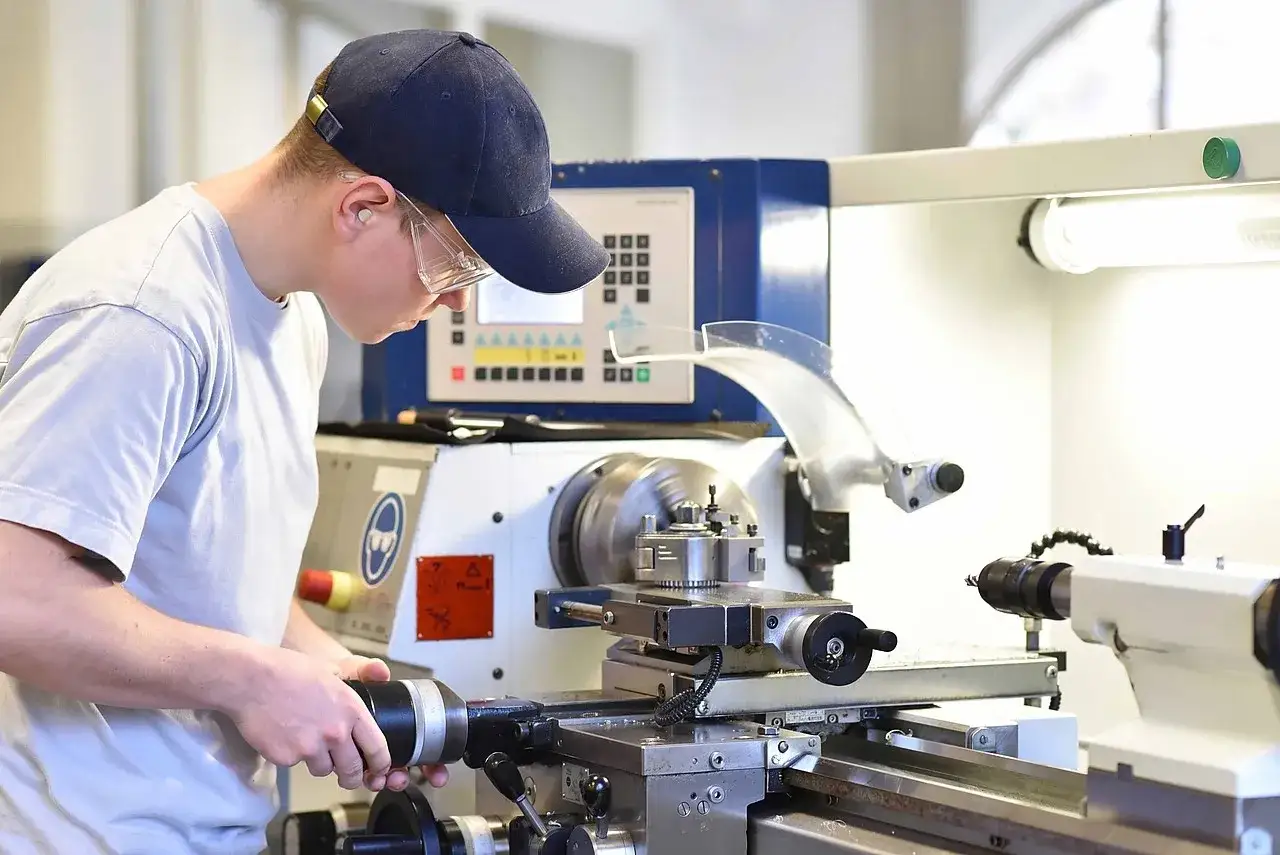 Junger Mann mit Schutzausr&uuml;stung bedient Drehmaschine. Er erkundet zerspanungsmechaniker weiterbildungsm&ouml;glichkeiten.