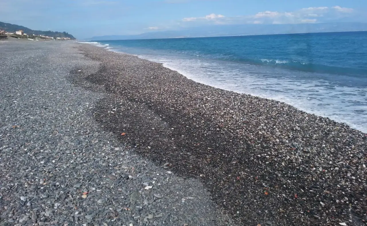 La spiaggia di Roccacalumera, con i suoi ciottoli scuri e il mare azzurro, invita a una passeggiata rilassante.