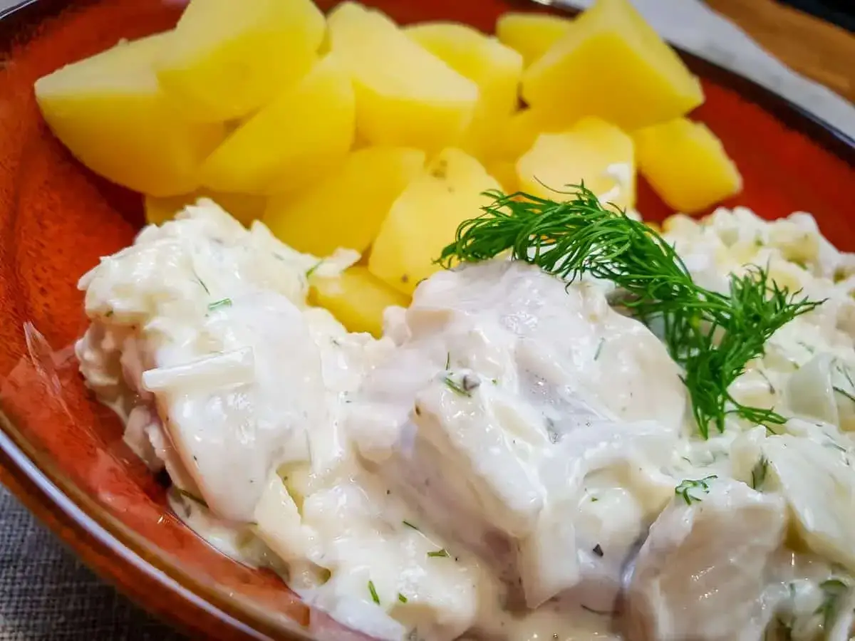 Pyszne śledzie w śmietanie z koperkiem, podane z gotowanymi ziemniakami. Klasyka polskiej kuchni.