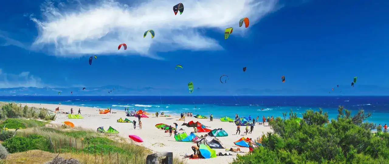 Bunte Kiteschirme tanzen am Himmel &uuml;ber dem Strand von Tarifa, Spanien. Menschen genie&szlig;en die Sonne und das Meer.