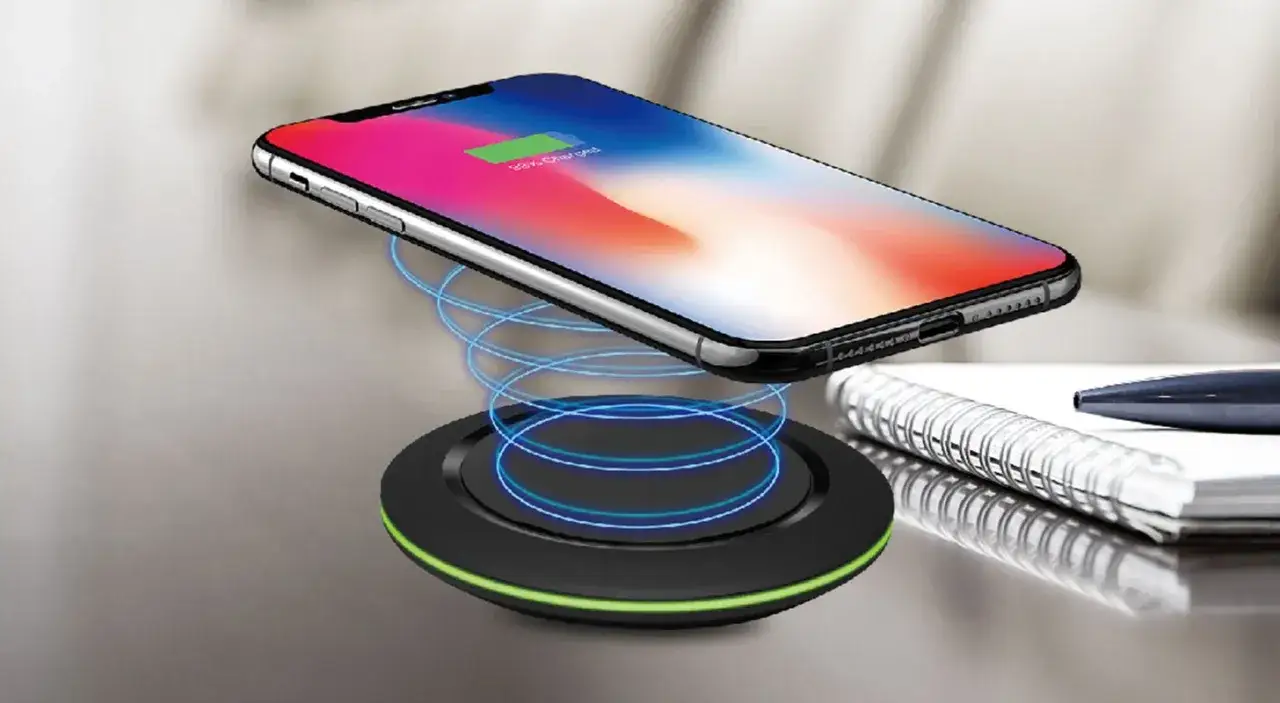 En iPhone laddas tr&aring;dl&ouml;st p&aring; en laddningsplatta. Bredvid ligger en anteckningsbok och en penna.