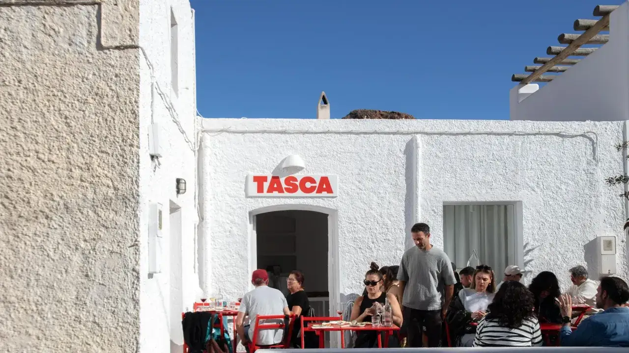 Gente disfrutando en el bar Tasca, con sus hortichuelas altas y el sol brillando.