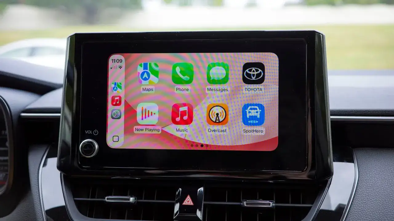 Ekran samochodu z ikonami aplikacji, pokazujący jak działa CarPlay. Widoczne ikony: Maps, Phone, Messages, Toyota, Now Playing, Music, Overcast, SpotHero.