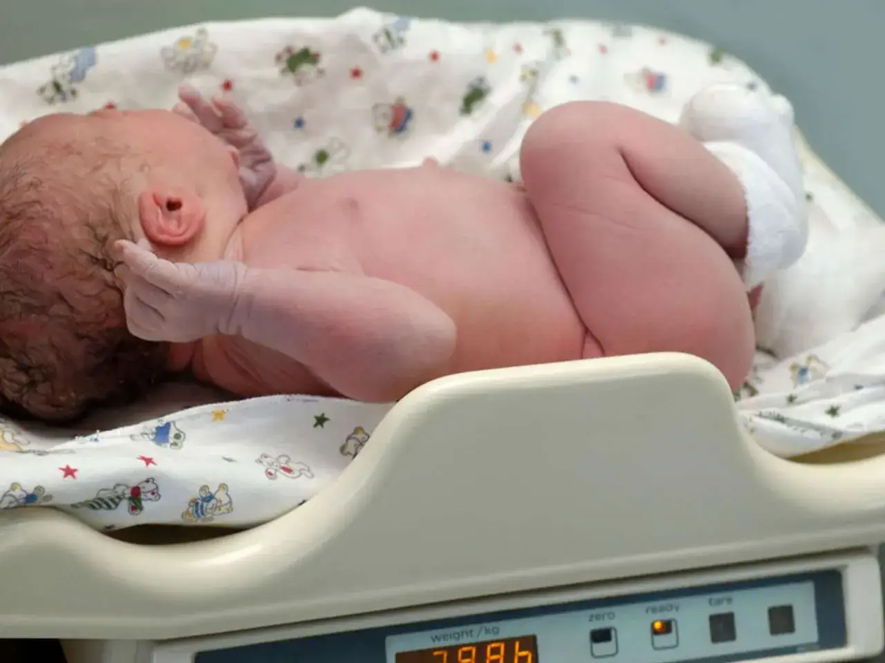 Neugeborenes Baby auf einer Waage, das sein Geburtsgewicht von 3,98 kg ermittelt.
