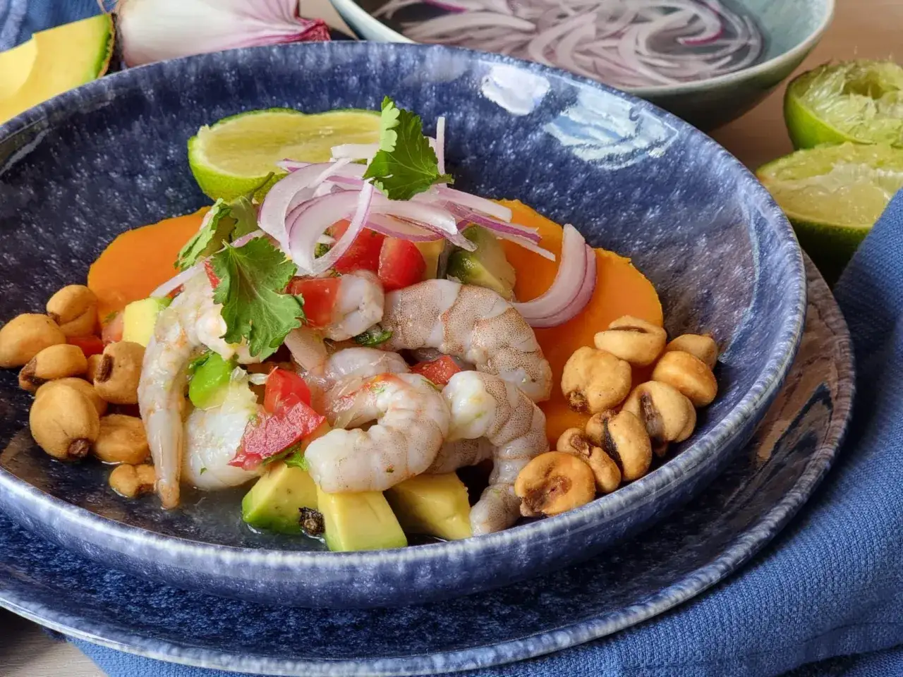 Delicioso ceviche de gambas con aguacate, tomate, cebolla morada, camote y cancha serrana en un taz&oacute;n azul.