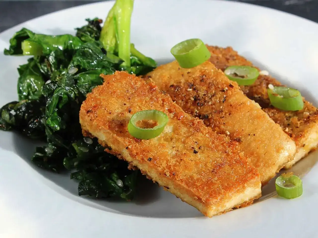 Knusprig paniertes Tofu auf einem Teller mit gedünstetem grünen Gemüse, garniert mit Frühlingszwiebelringen. Perfekt für Tofu panieren.