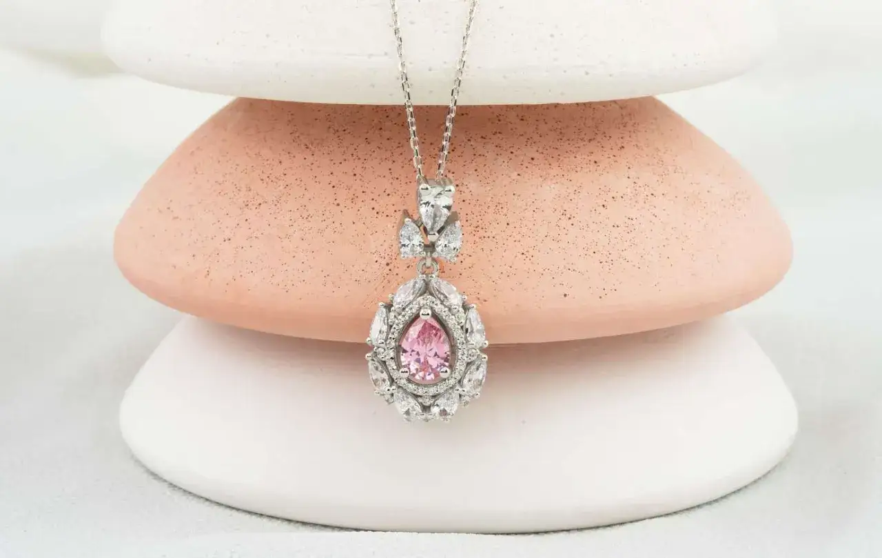 Ein zartes Collier mit einem tropfenförmigen rosa Saphir, umgeben von funkelnden Zirkonia. Die Bedeutung von rosa Saphir steht für Liebe und Mitgefühl.