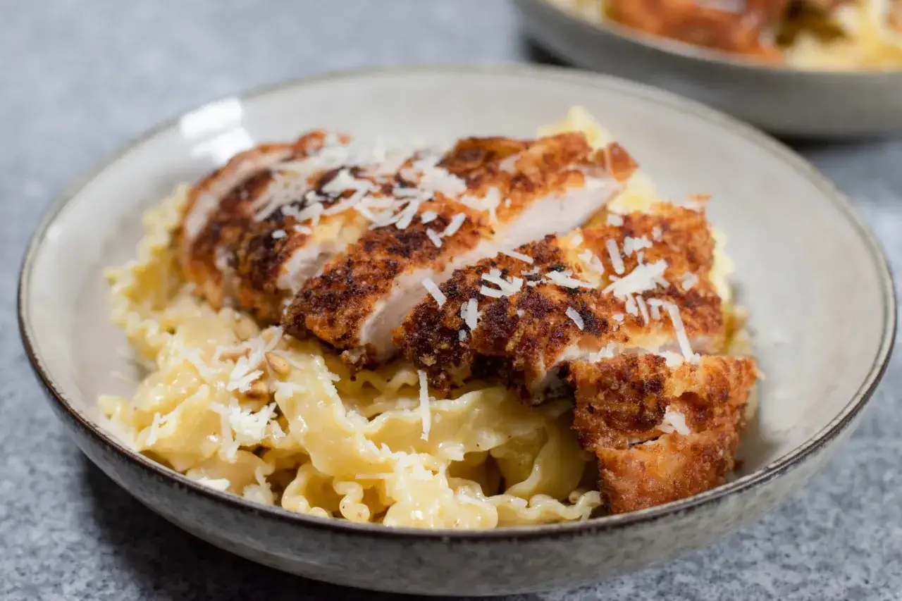 En sk&aring;l med kr&auml;mig pasta alfredo kyckling, toppad med riven parmesan.