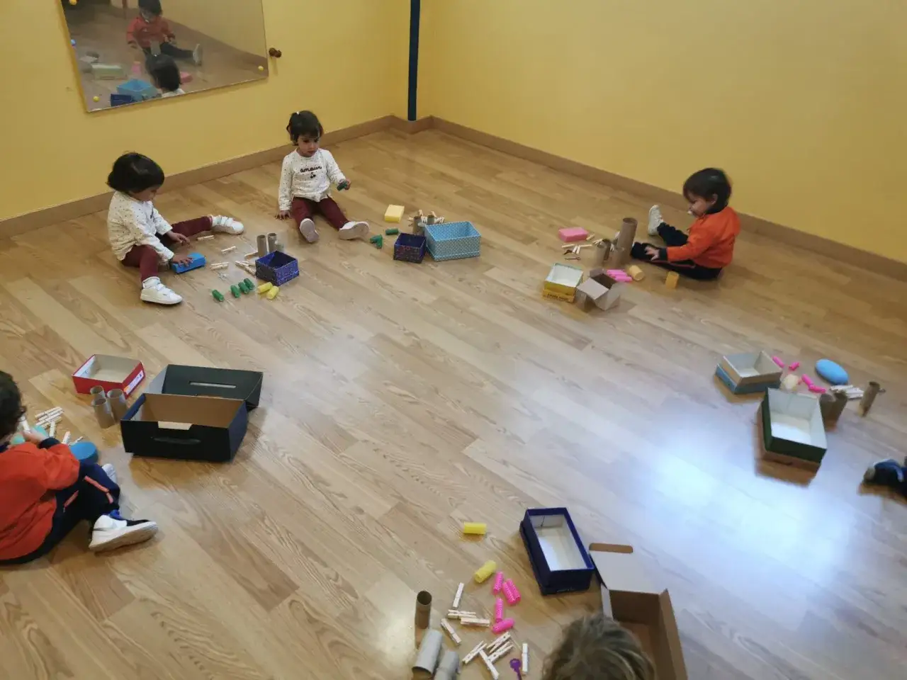 Niños pequeños exploran materiales diversos, cajas y pinzas, aprendiendo sobre el juego heurístico.