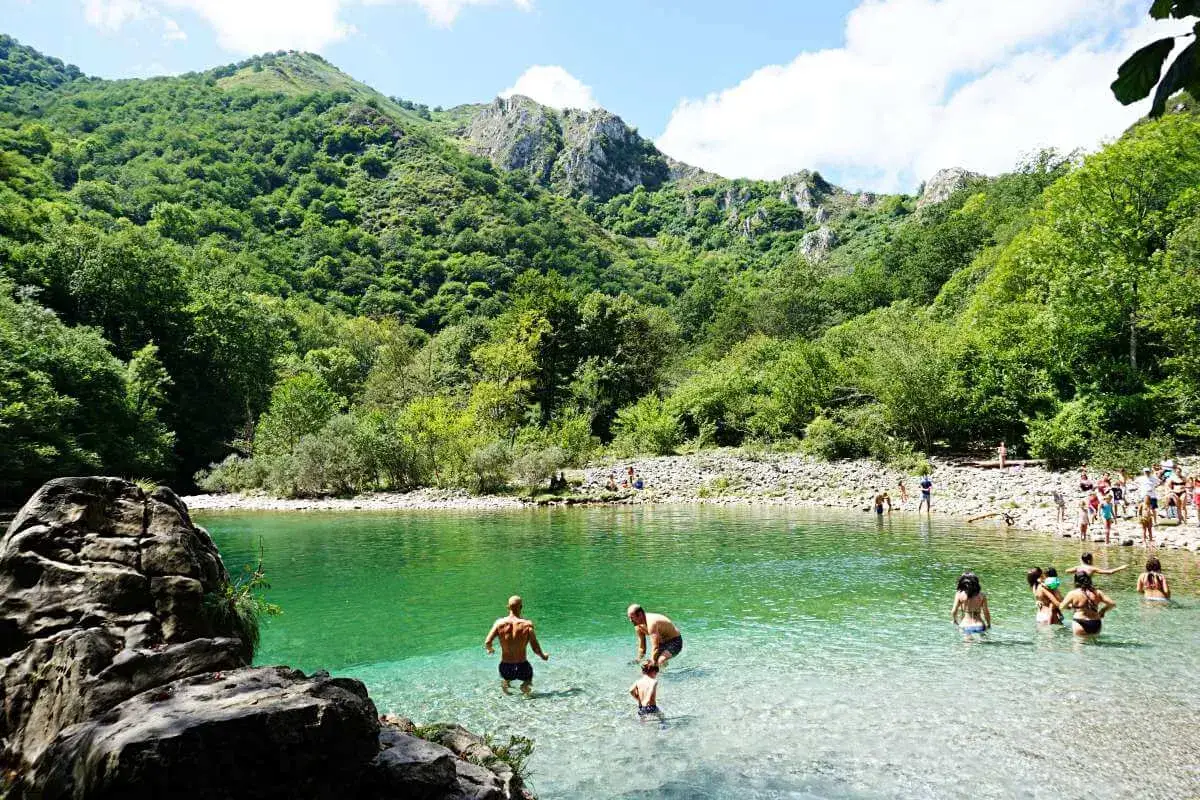 Gente disfrutando del agua cristalina en la senda de la hoya de san vicente, rodeada de exuberante vegetación y montañas.