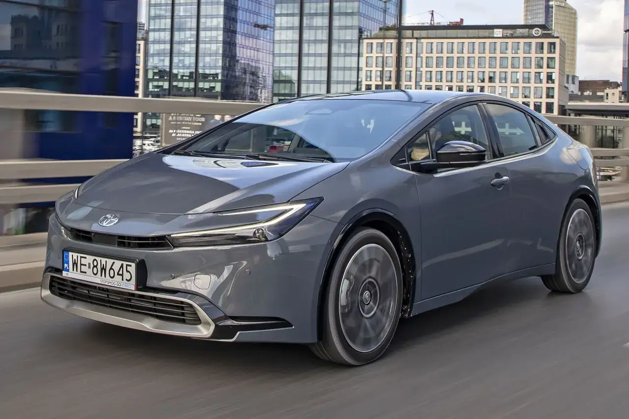 Szary Toyota Prius jedzie przez miasto, mijając nowoczesne budynki.