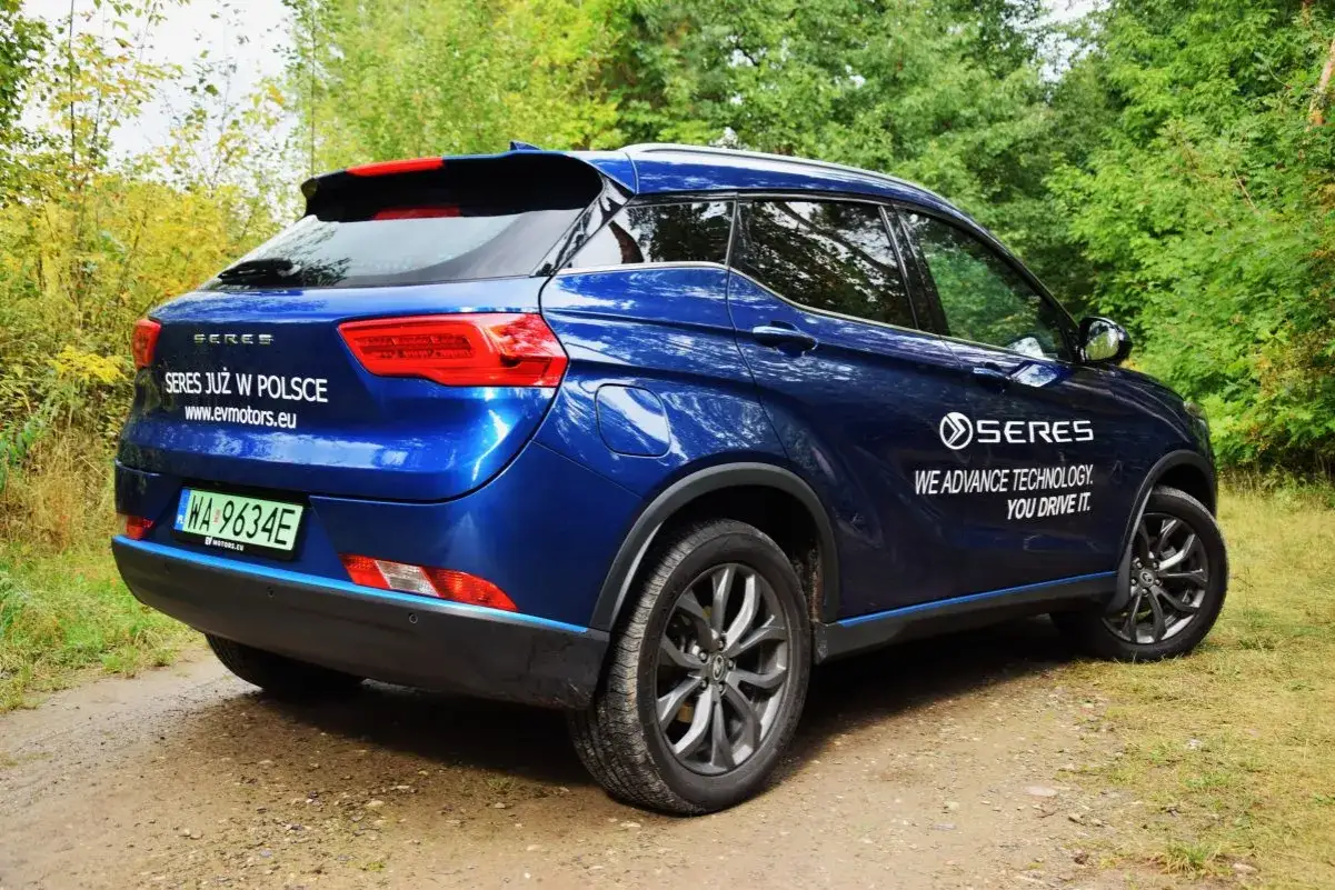 Niebieski SUV Seres 3 stoi na leśnej drodze. Na karoserii widnieje napis