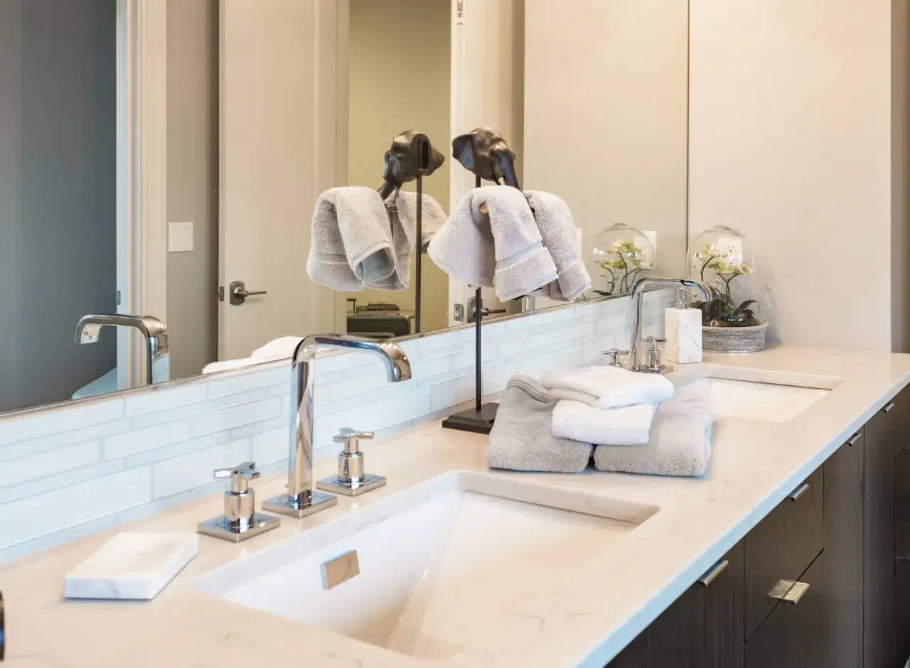 A modern bathroom vanity with a marble-look countertop, double sinks, and chrome fixtures. Freshly folded towels sit neatly on the surface, ready to replace bathroom countertop clutter.