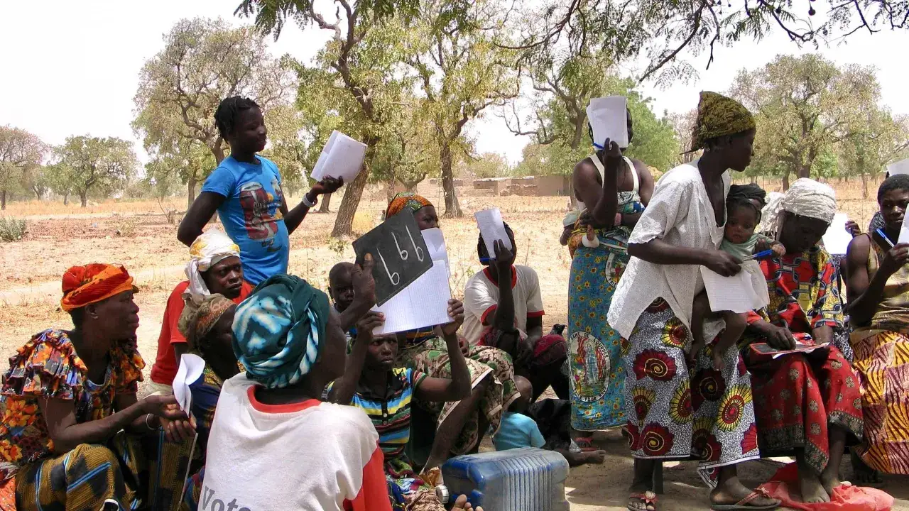 Grupa kobiet i dzieci w Burkina Faso uczy się na zewnątrz, trzymając papier i tabliczki.