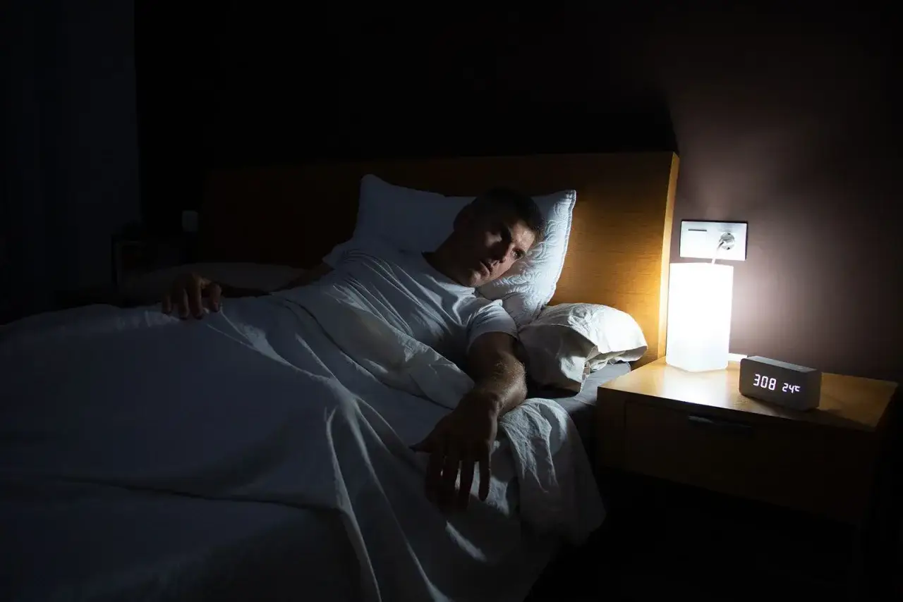 Mann liegt im Bett, kann nicht schlafen. Die Nacht ist dunkel, nur ein Nachttischlicht brennt. Er ist wach und starrt ins Leere.