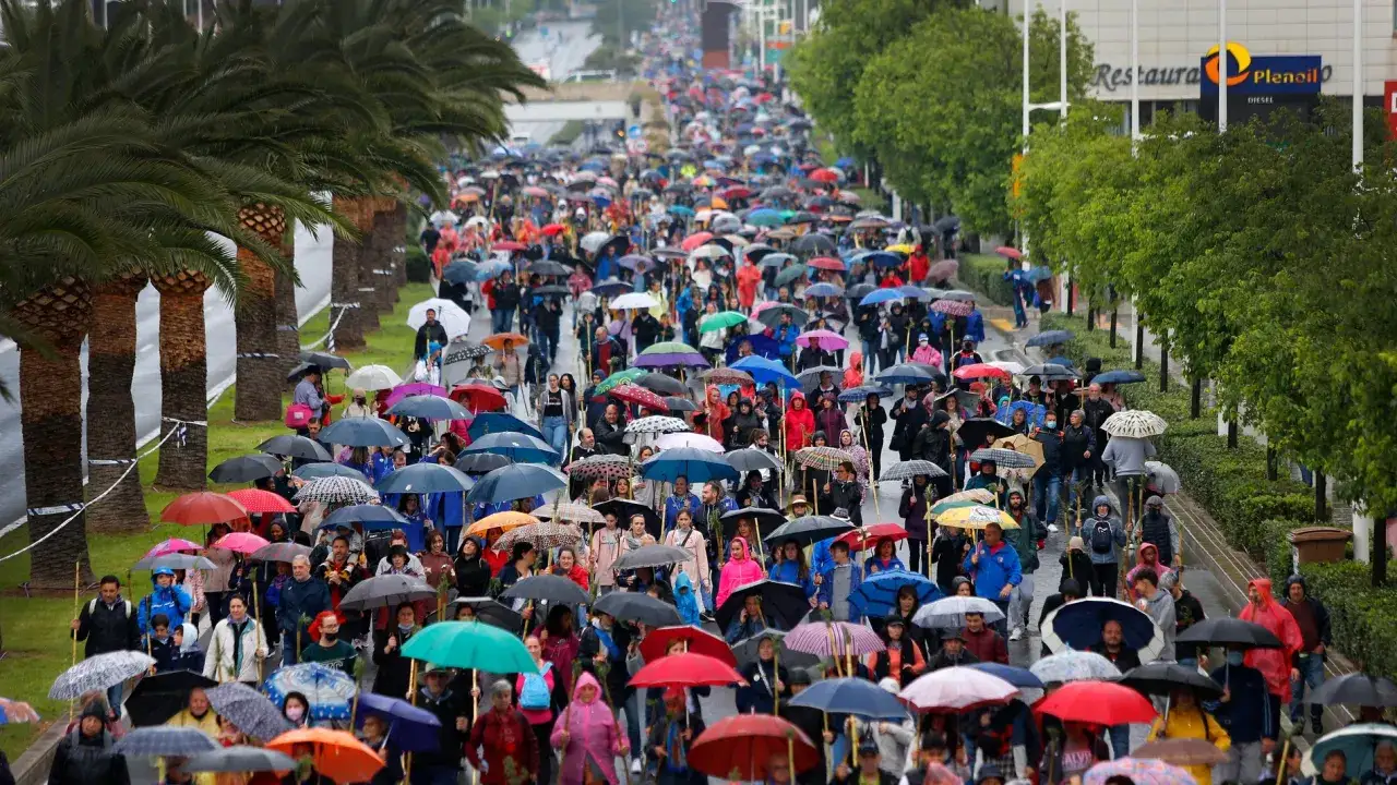 Multitudinaria romería de la Santa Faz avanza bajo la lluvia, protegida por paraguas de colores.