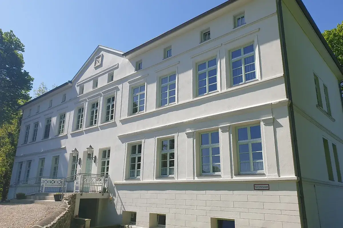 Das Herrenhaus Blengow, ein weißes Gebäude mit vielen Fenstern, steht unter blauem Himmel.