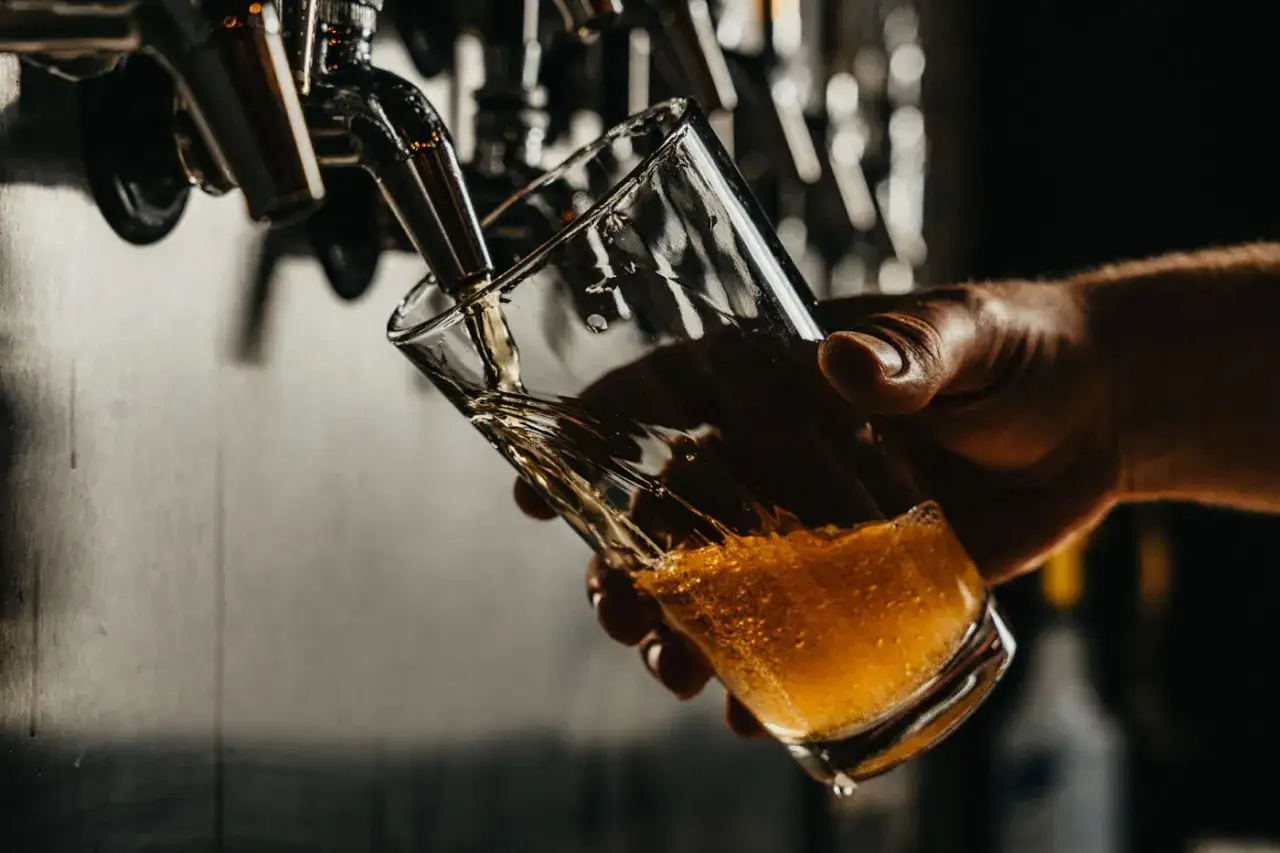 Mano che versa birra in un bicchiere. La schiuma indica che la birra &egrave; andata a male, con un aspetto torbido e poco invitante.