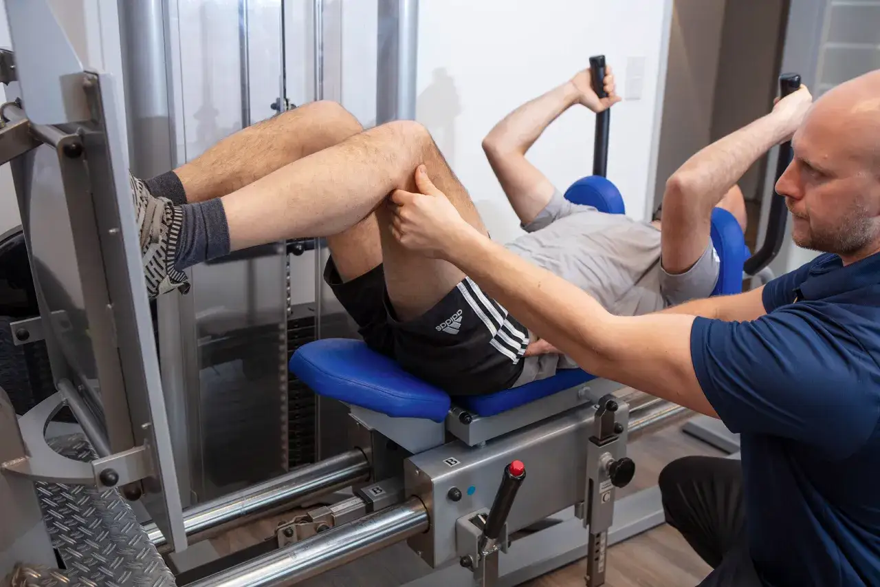 Mann auf Beinpresse, Physiotherapeut gibt Anweisungen. Ein typisches KGG Rezept für Reha.