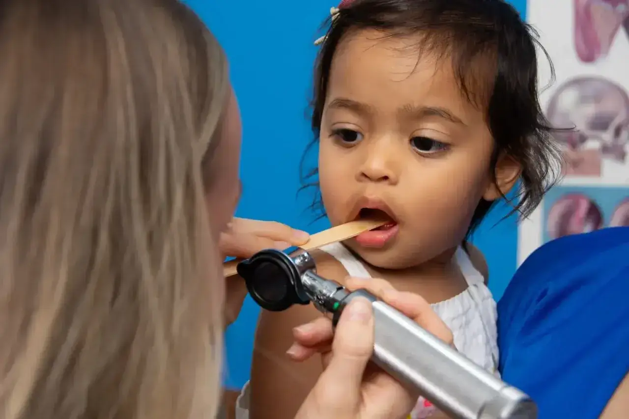 Medico esamina la gola di una bambina con abbassalingua e otoscopio. Un controllo per il mal di gola bambini.