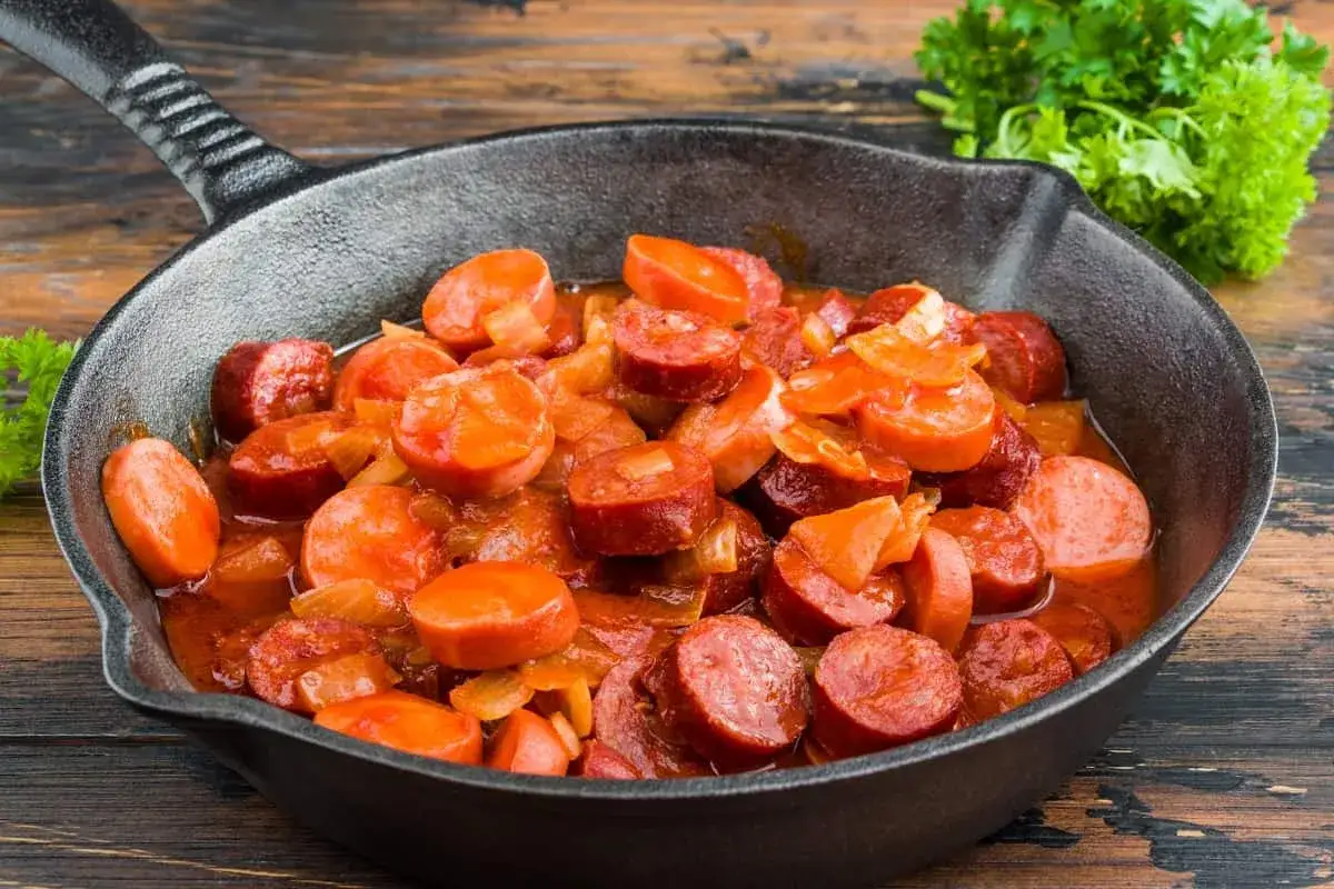 Salchichas en salsa roja, cortadas en rodajas y cocinadas en una sart&eacute;n de hierro fundido, con perejil fresco al lado.