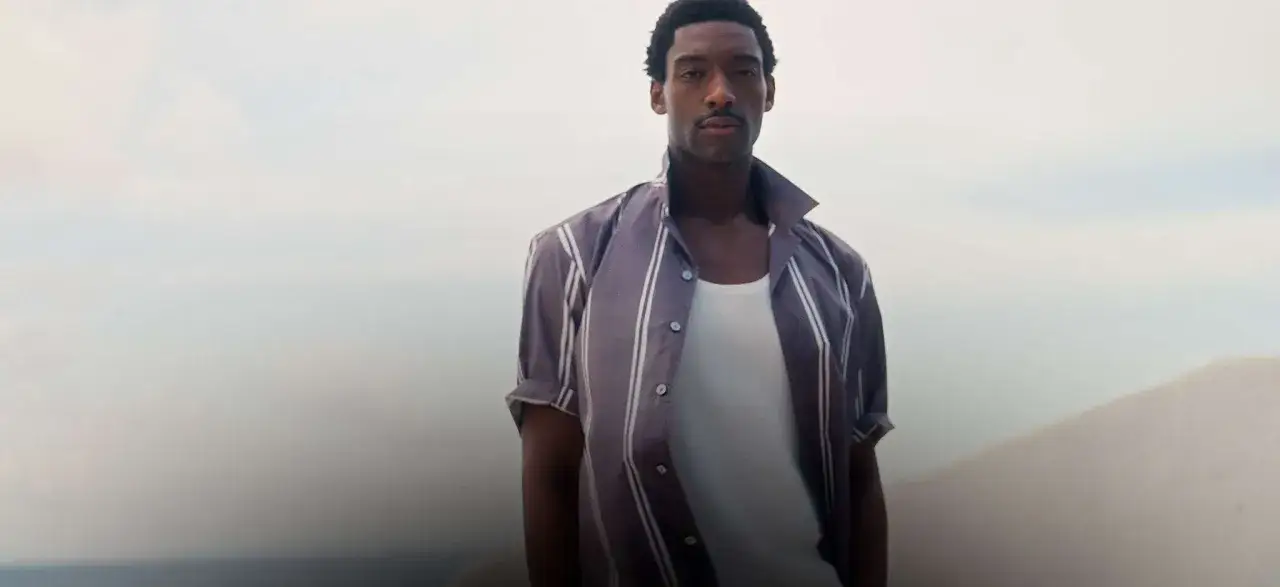 Uomo con baffi indossa camicia a righe e canotta bianca, un look che fa pensare alla differenza tra Hugo e Boss.
