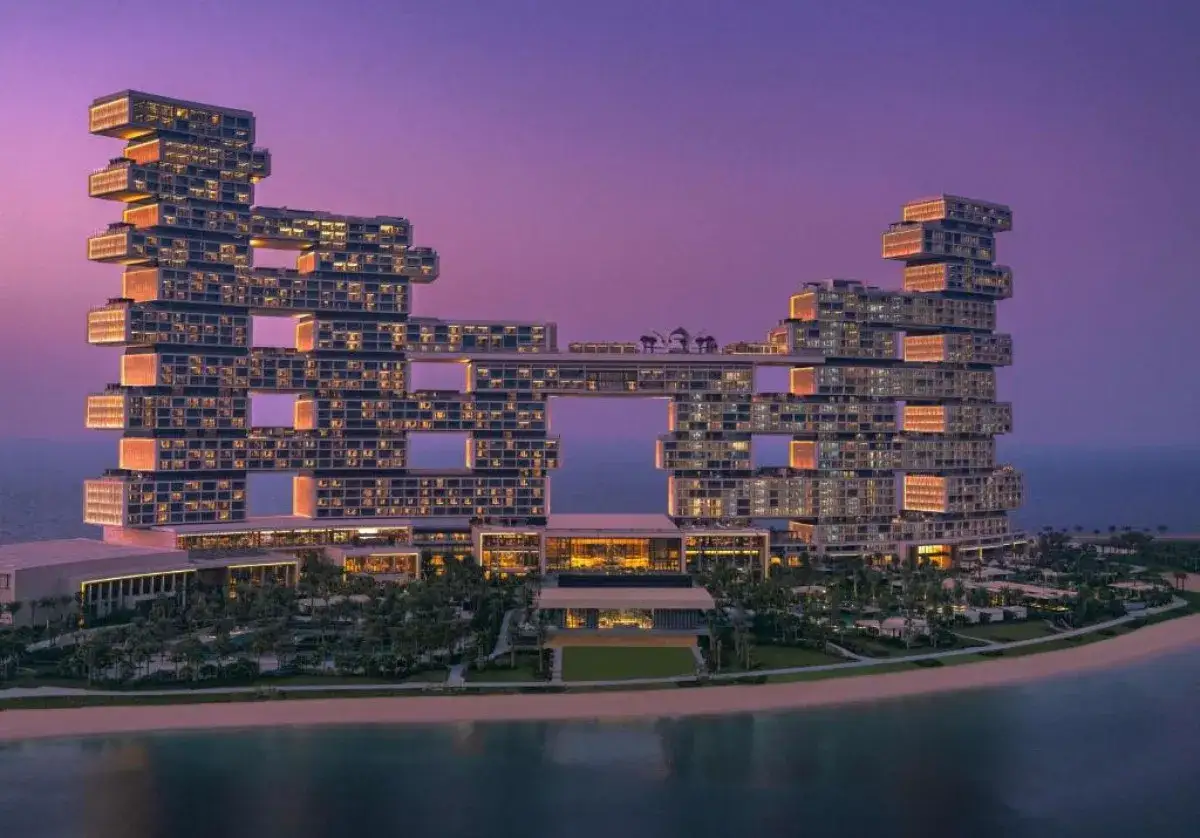 Najdroższy hotel w Dubaju, Atlantis The Royal, lśni nocą na tle fioletowego nieba. Jego architektoniczna forma przypomina kaskadę bloków.